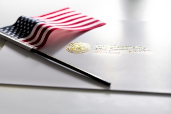 U.S. Citizenship and Immigration Services envelope, white folder for naturalization certificate on table with American flag
